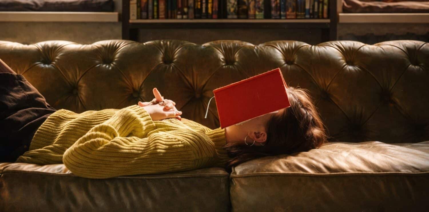 women lying on a sofa with book on face having a nap