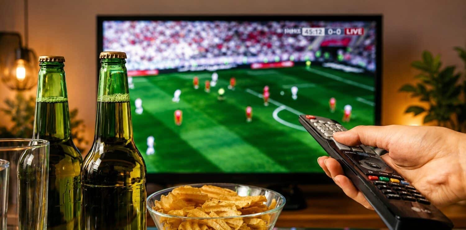 A person watching football on tv with beers and snacks