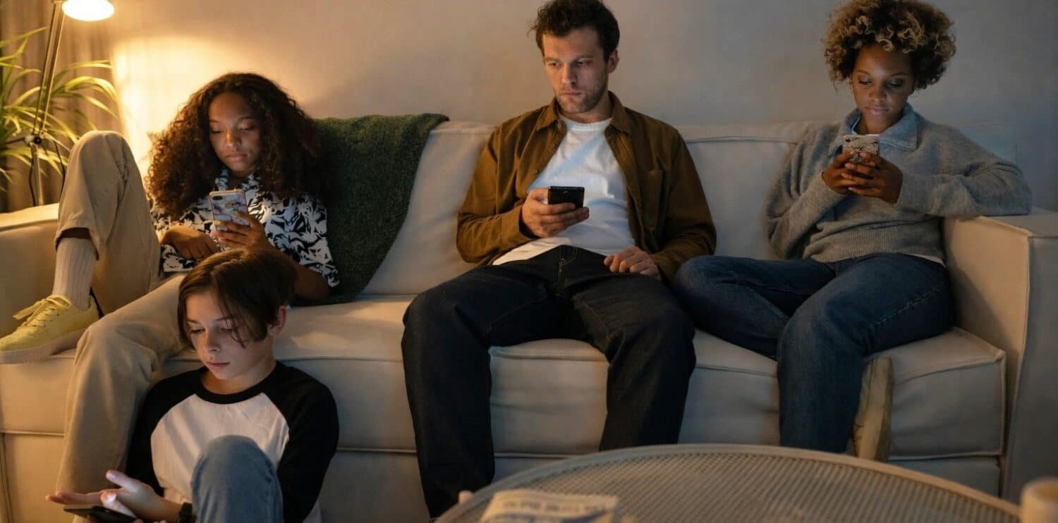 family sitting on the sofa, all staring at their mobile phones.