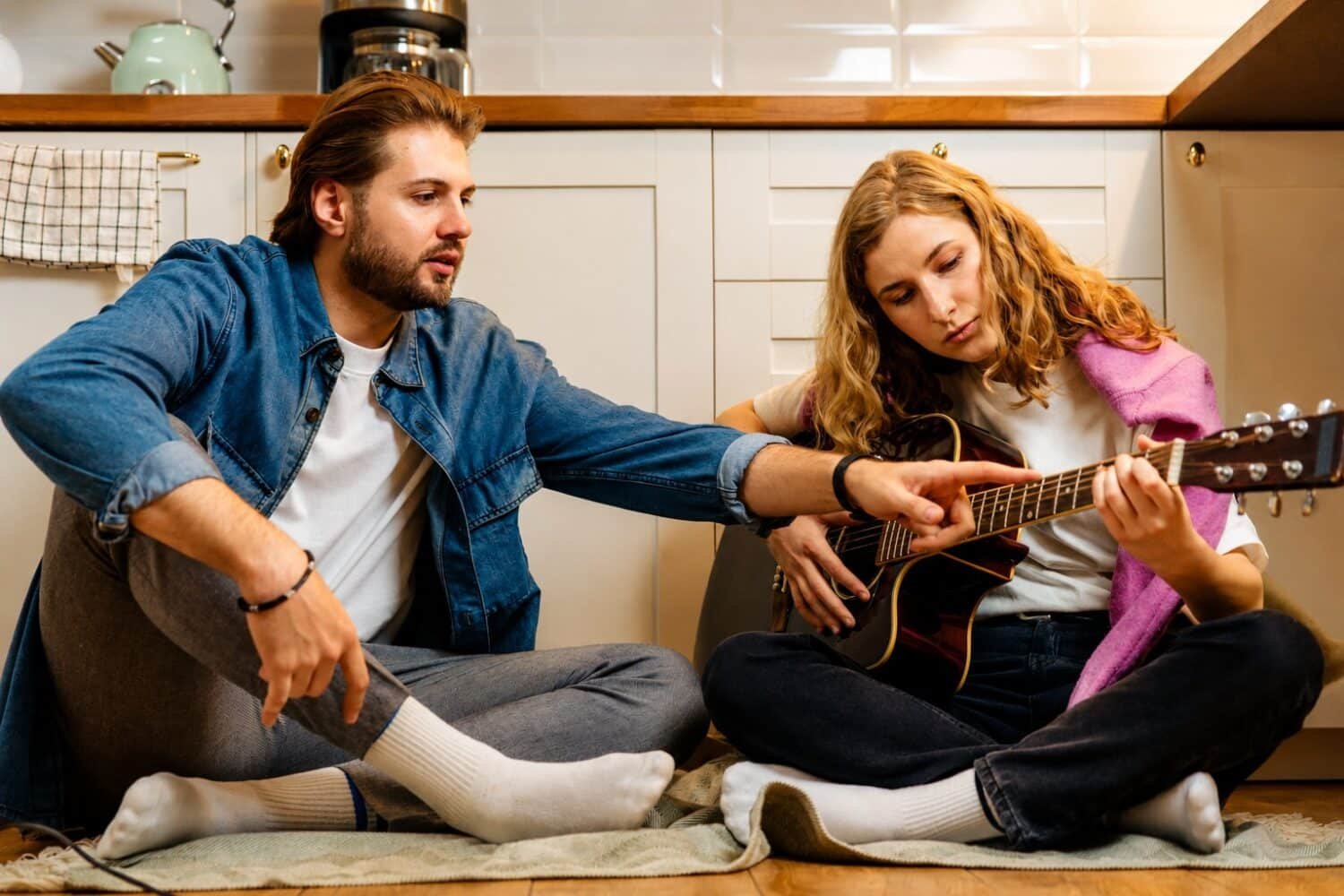 man teaching women to play guitar whilst sat on the kitchen floor